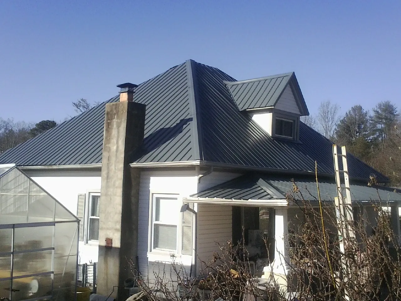 Dark blue standing seam metal roof on a white farmhouse with dormer — Slate & Tile Roof Repair by Roofing Brothers in Willseyville