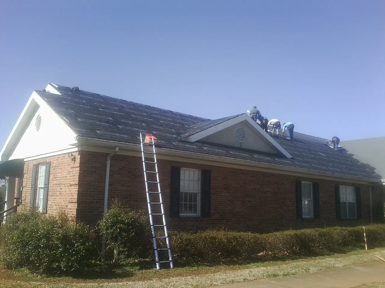 Crew tearing shingles off a brick ranch roof with a ladder set — Emergency Roof Repair work by our crew in Willseyville