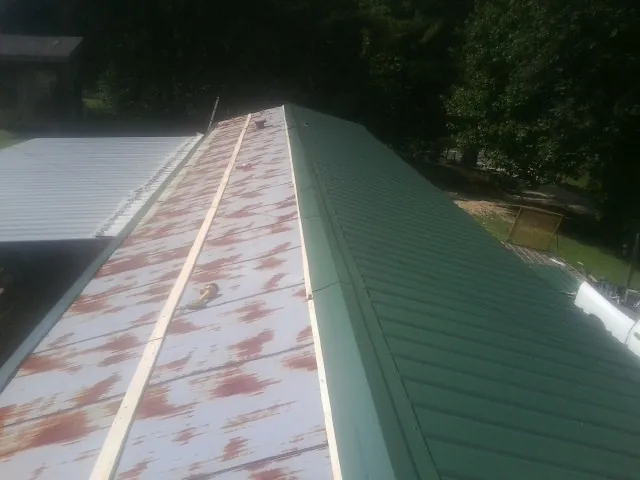 Old rusted panels beside newly installed green metal roofing — Wind Damage Roof Repair by Roofing Brothers in Willseyville