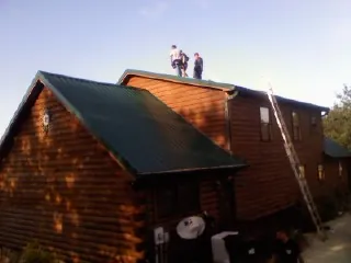 Crew on the ridge of a green metal roof on a two story log home in Willseyville