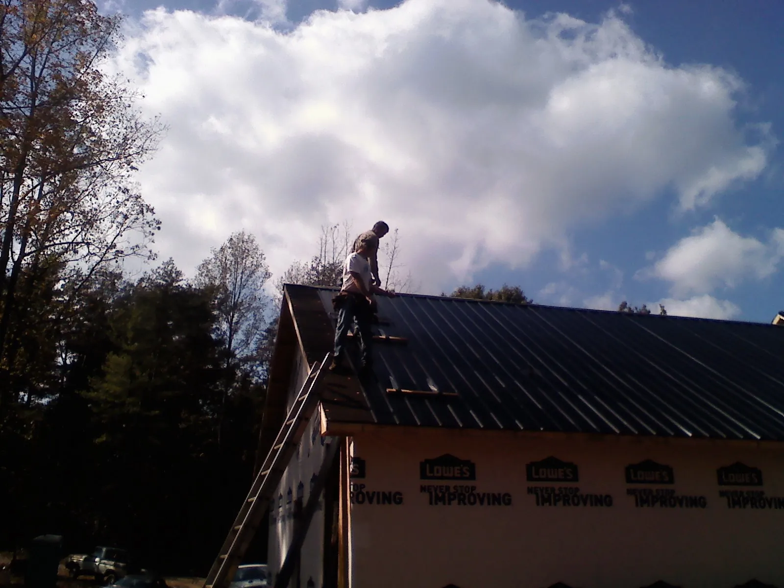 Roofer fastening dark metal panels high against a cloudy sky, from a Roof Inspection job in Willseyville
