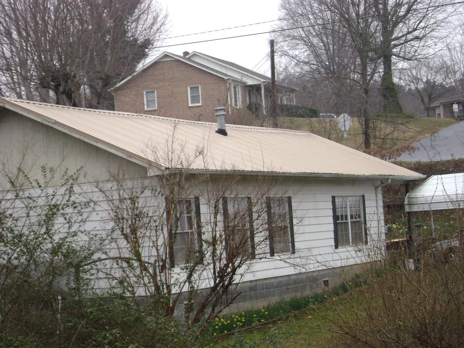Tan metal roof on a white sided house set into a hillside — Commercial Roofing by Roofing Brothers in Willseyville